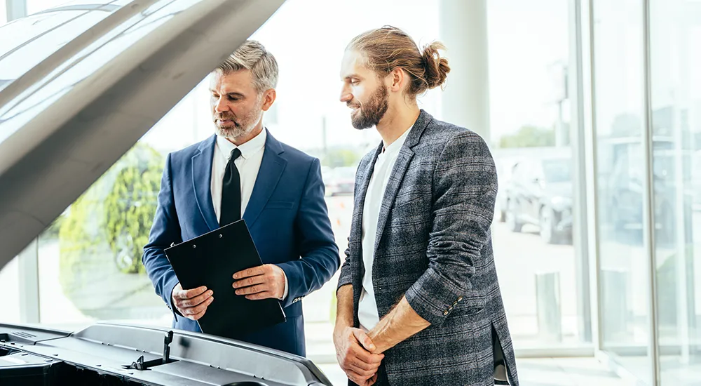 Verkäufer im Autohaus mit Kunden vor einem Auto